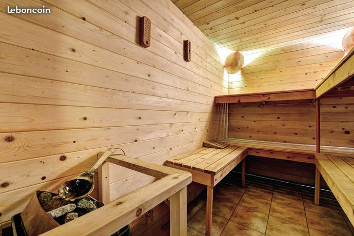 A wooden sauna interior features smooth paneling and stone accents, creating a warm and relaxing environment. Wooden benches line the walls, providing seating. Natural light casts a soft glow, highlighting the earthy tones of the space.