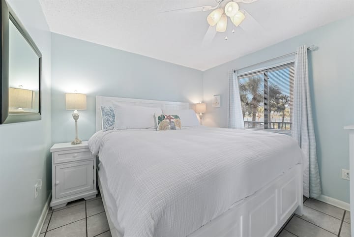 Rudi kwenye chumba cha kulala cha msingi chenye utulivu na starehe. Sehemu hii tulivu ina kitanda cha ukubwa wa kifalme na muundo safi, uliohamasishwa na pwani, unaofaa kwa ajili ya kulala kwa utulivu usiku.