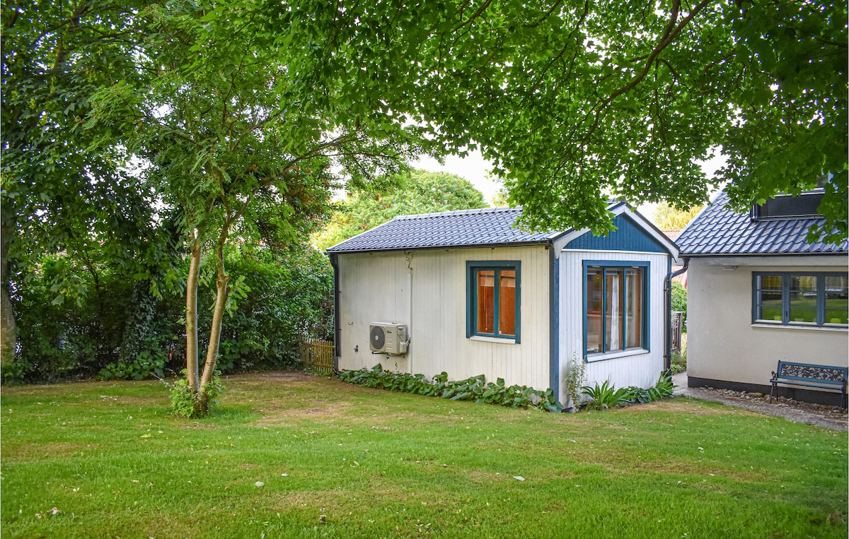 A quaint vacation apartment is nestled among lush green trees, offering a peaceful exterior view. Bright windows allow natural light to enter, while greenery and well-kept grass surround the property, creating a serene outdoor space.