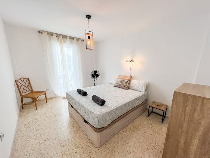 Habitación con salida a un pequeño balcón con cama de 160cm. Mesillas de noche. Silla de madera y mueble de almacenaje. 