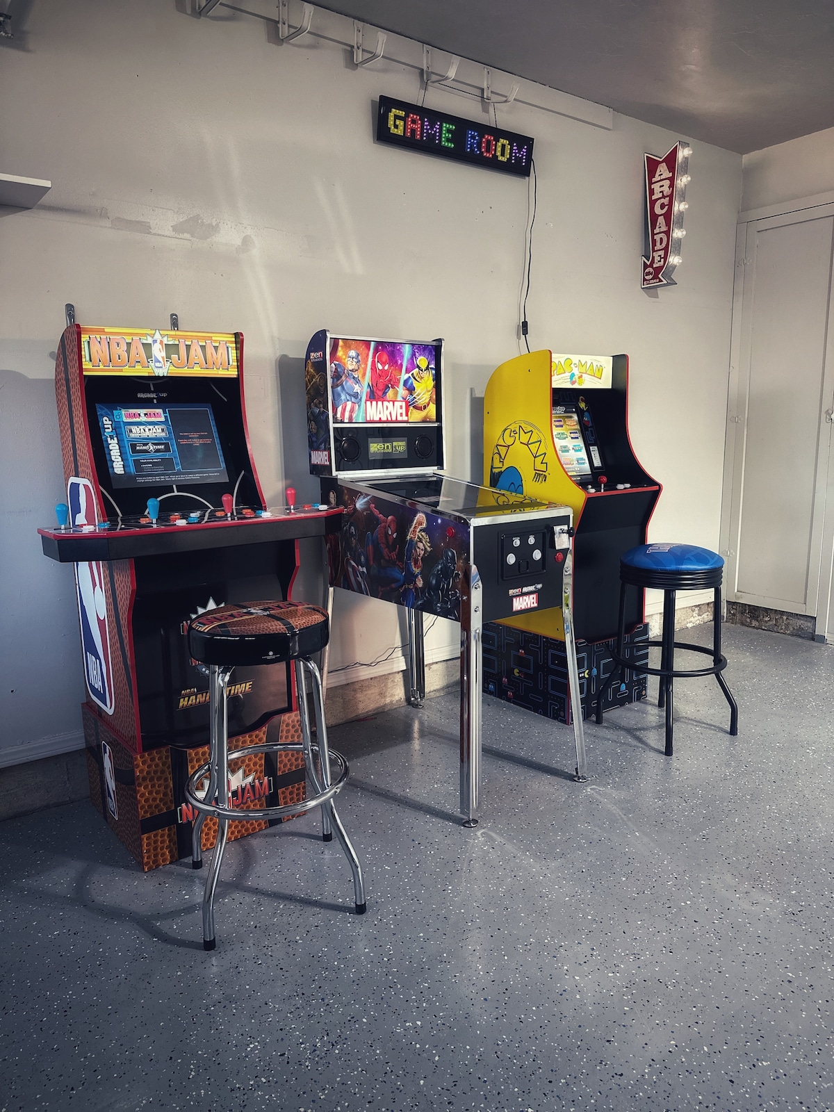 An arcade game area is showcased with three retro-style machines, including NBA Jam and Marvel-themed games. Stools are positioned next to the machines, and a sign reading 'GAME ROOM' is displayed above, contributing to a fun gaming environment.
