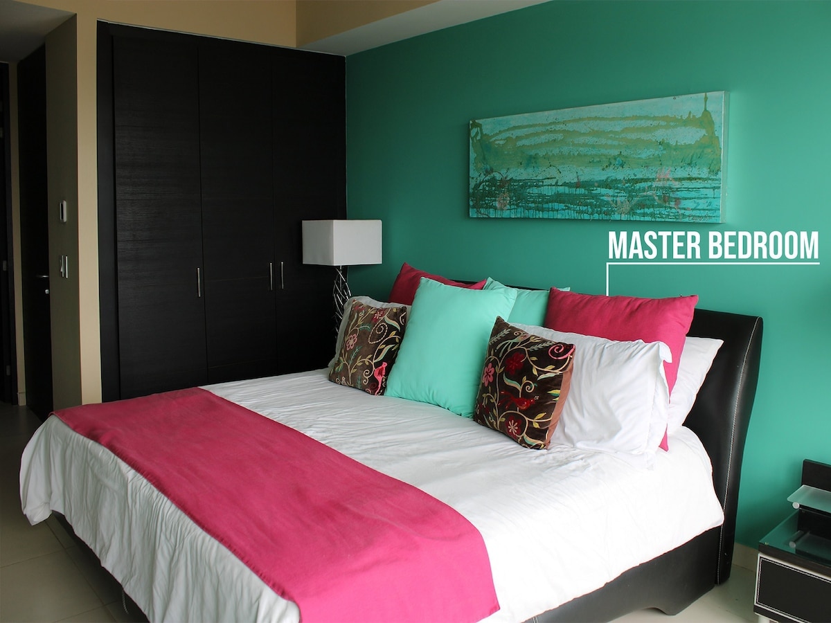 Dormitorio principal con una lujosa cama king, una audaz pared decorativa y acceso al balcón para disfrutar de unas vistas impresionantes.