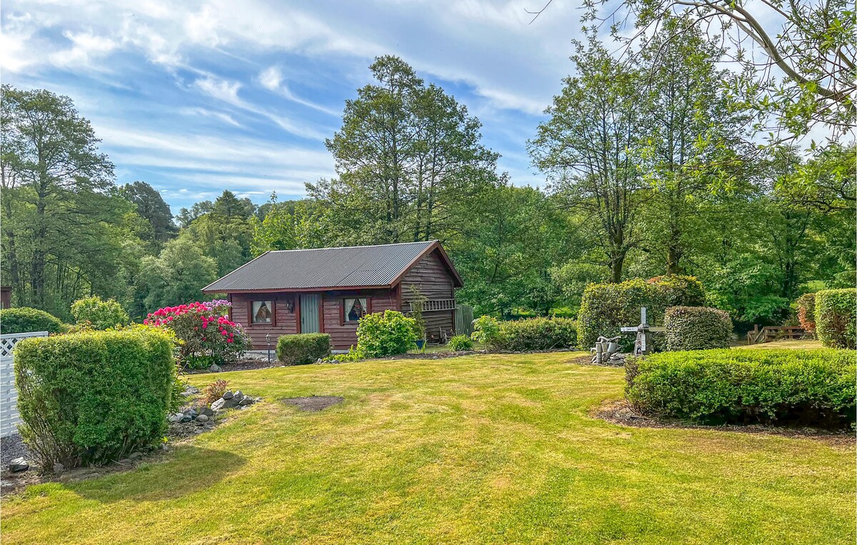 A classic wooden house is set within a large, well-maintained garden, surrounded by lush greenery. Trimmed hedges and vibrant flowerbeds frame the property, while a clear blue sky enhances the serene atmosphere of the natural landscape.