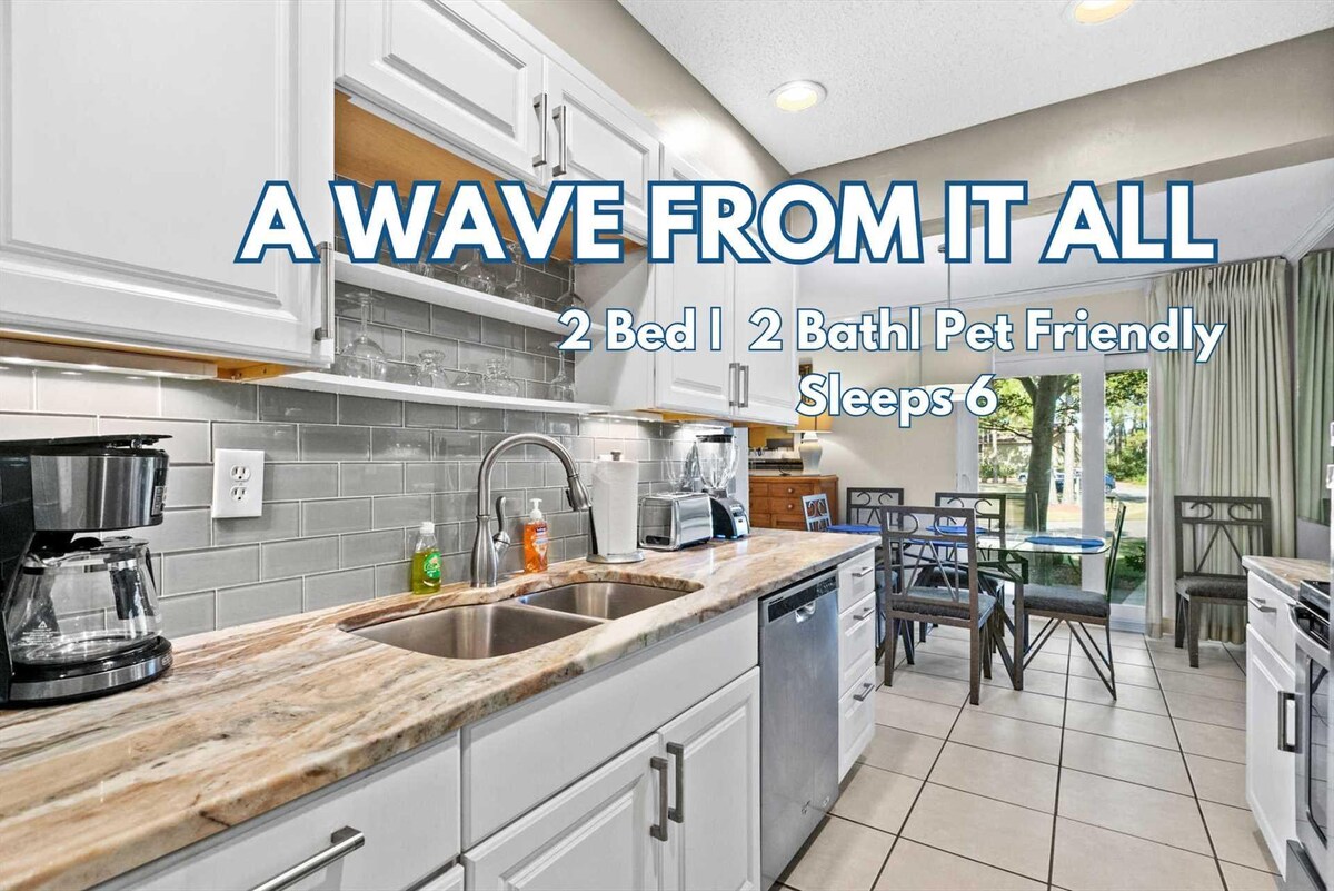 The kitchen features white cabinets and a marbled countertop, complemented by stainless steel appliances including a coffee maker. A dining table is positioned near a window, allowing natural light to brighten the space. The layout encourages a functional and inviting cooking area.