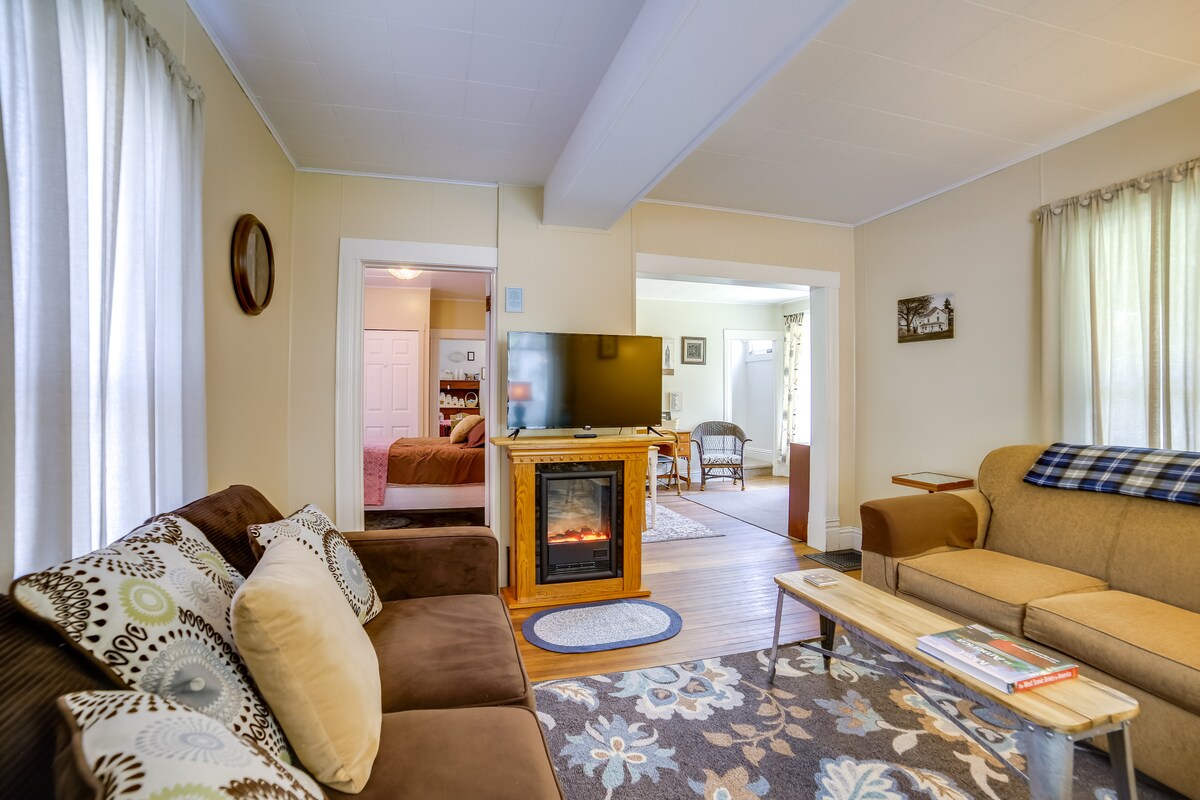 A comfortable living area features a cozy couch and a decorative chair, complemented by a soft area rug. An electric fireplace adds warmth, while large windows allow natural light to fill the space. The open layout leads to the dining area and additional rooms.