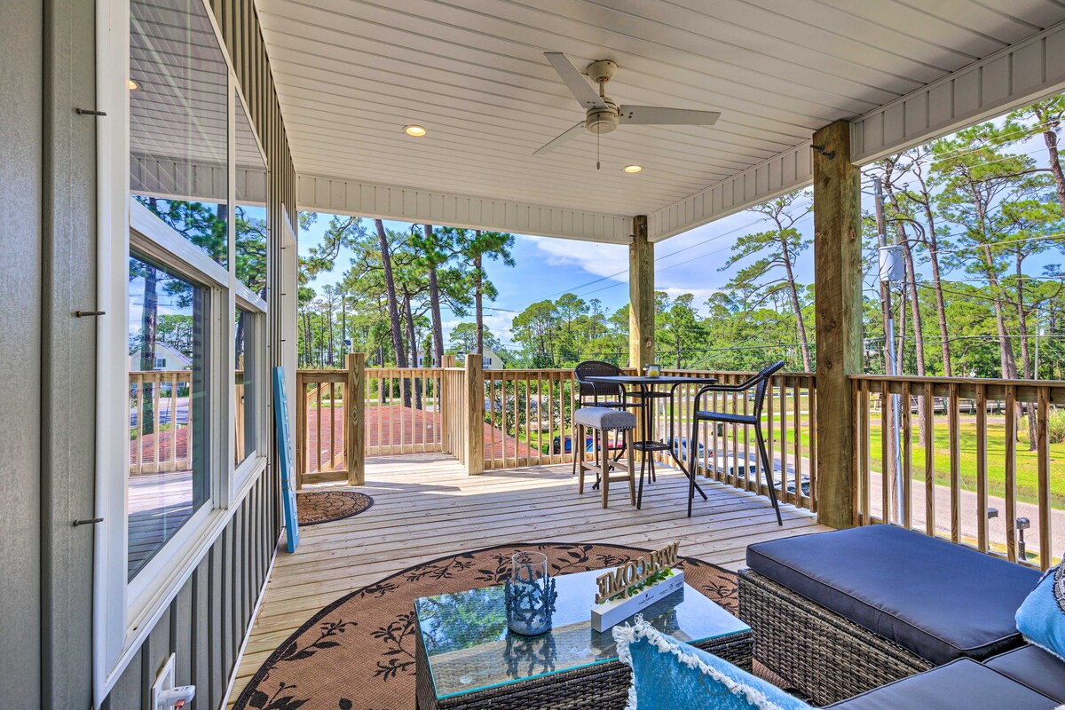 A spacious outdoor balcony area is equipped with seating, featuring a small table and bar stools. A comfortable lounge section is adorned with blue accents. The surrounding trees provide a natural backdrop, while the open layout allows for light and air to flow freely.