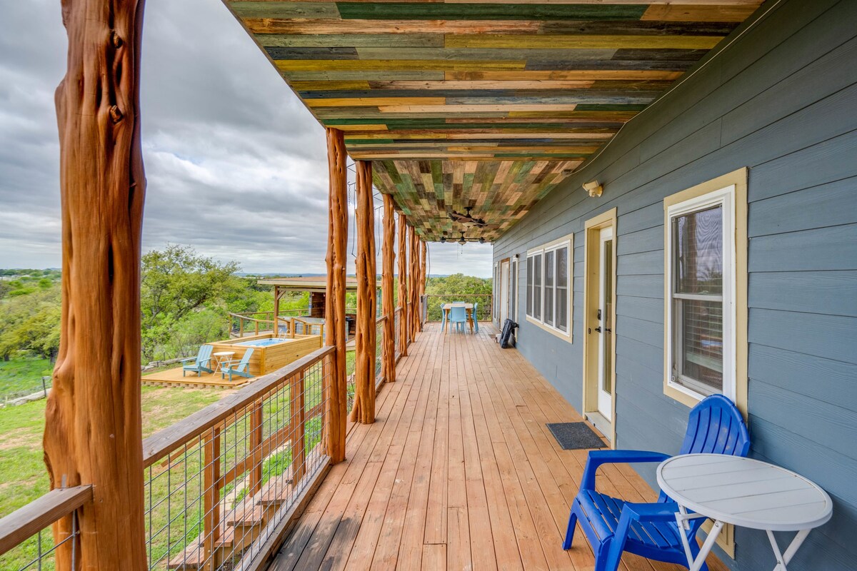 A spacious outdoor deck features a rustic wooden ceiling and sturdy wooden beams. Blue chairs are positioned alongside a small white table, providing a relaxing spot. The expansive views of the surrounding landscape enhance the outdoor experience, while the deck's polished wood surface extends toward the horizon.