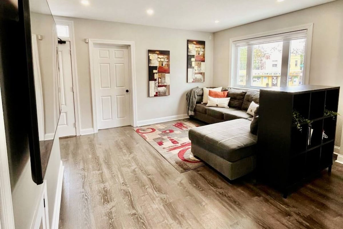 The inviting living area features a spacious sectional couch in a neutral tone, accompanied by decorative pillows. A vibrant area rug adds color to the floor, while wall art enhances the atmosphere. Natural light streams in through large windows, illuminating the open layout.