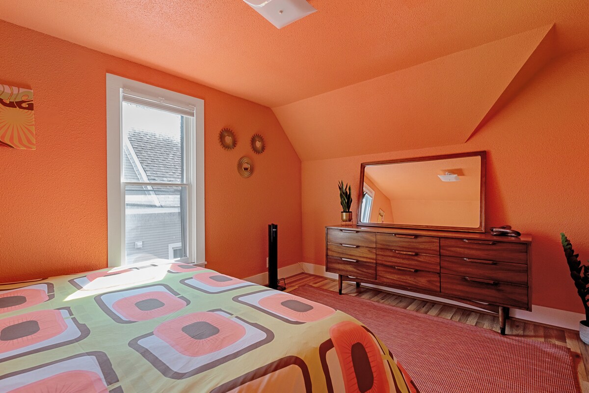 La chambre 1 dispose d'un lit king size au design rétro, accentué dans une orange vif, créant une atmosphère chaleureuse et accueillante.