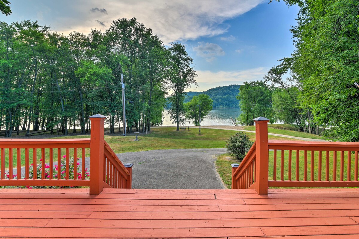 A view from the wraparound deck showcases the serene landscape, featuring lush trees and ample outdoor space leading to the Ohio River. The vibrant red railing complements the natural surroundings, offering a welcoming sight for guests.