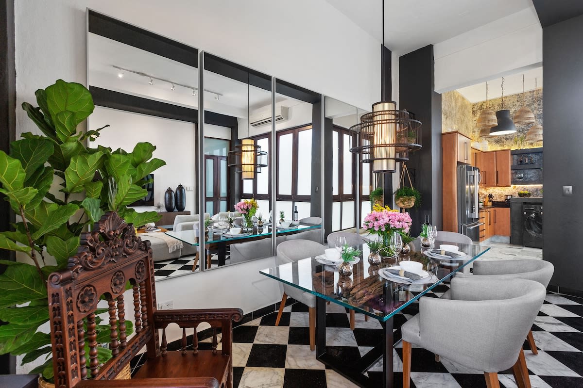 The dining area features a glass table surrounded by six upholstered chairs, complemented by a decorative wooden chair. A vibrant arrangement of flowers is placed at the center, while large mirrors and modern lighting enhance the space. The black and white checkered flooring adds contrast.