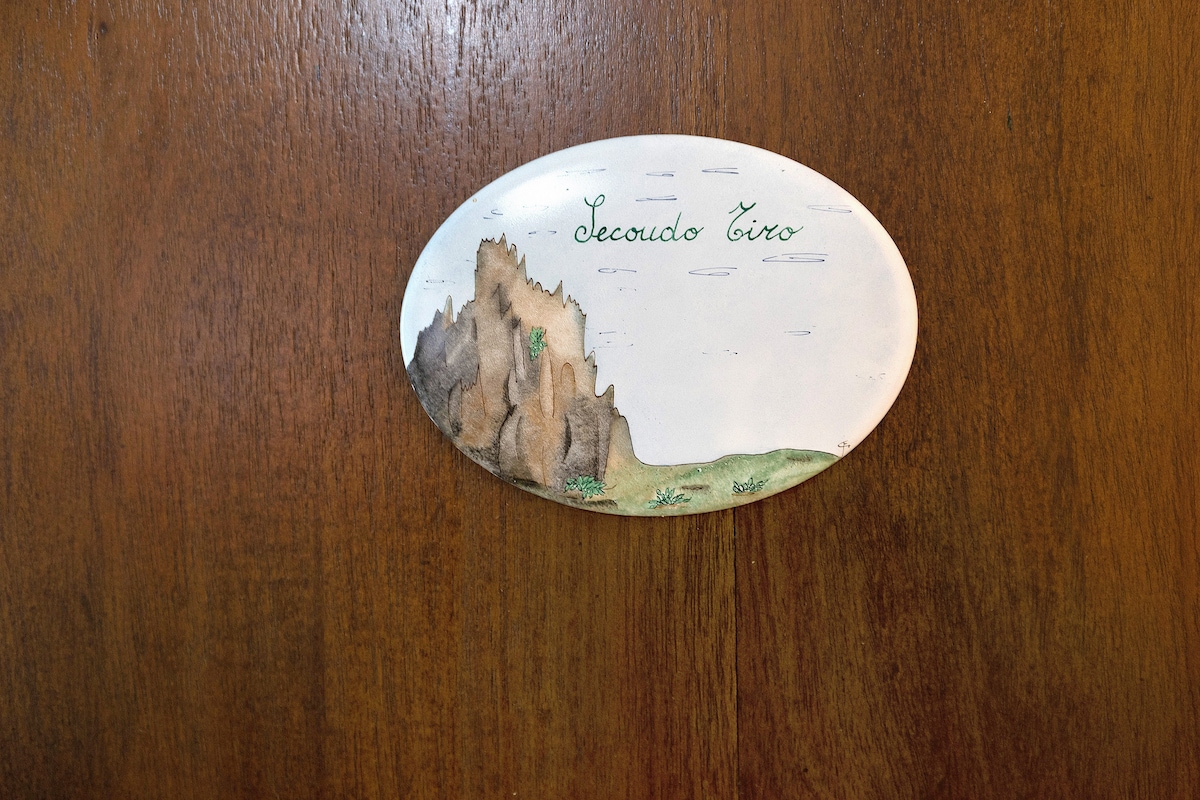 An artistic plaque displays the name 'Secondo Tiro' along with a scenic illustration of a rocky landscape. The plaque is affixed to a wooden surface, providing a rustic touch to the entrance.