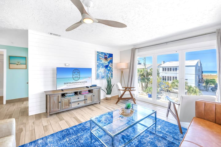 Светло жилищно пространство със смарт телевизор, стилен декор и големи прозорци с изглед към Сиеста Кий.