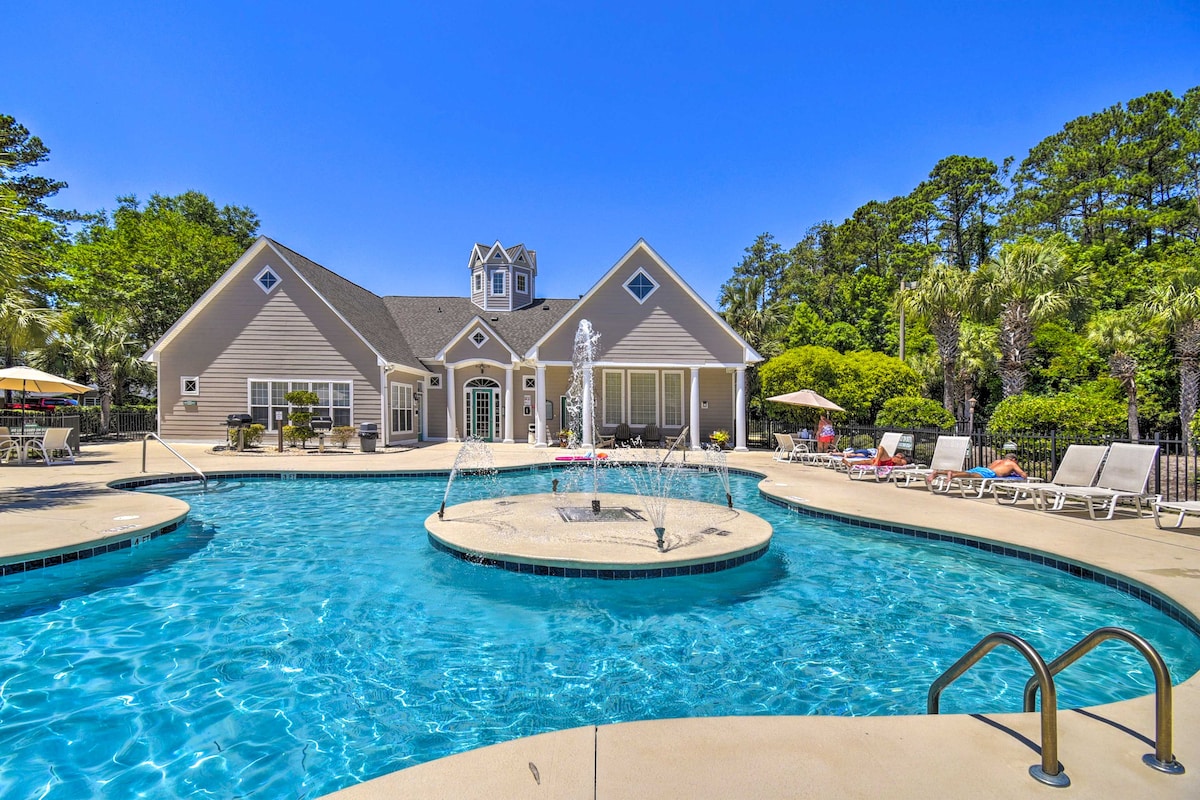 A community pool area is presented, featuring a circular water feature and a spacious deck. Lounge chairs are arranged around the pool, and the surrounding landscape includes greenery and palm trees, creating a relaxing ambiance for guests to enjoy.