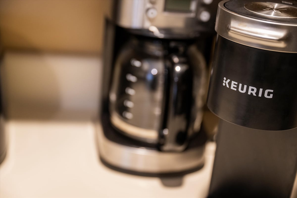 A coffee station is highlighted with a modern Keurig brewer alongside a traditional coffee maker. The sleek design of the appliances is complemented by a glass carafe, which reflects the surrounding light, creating a streamlined and functional coffee preparation area.