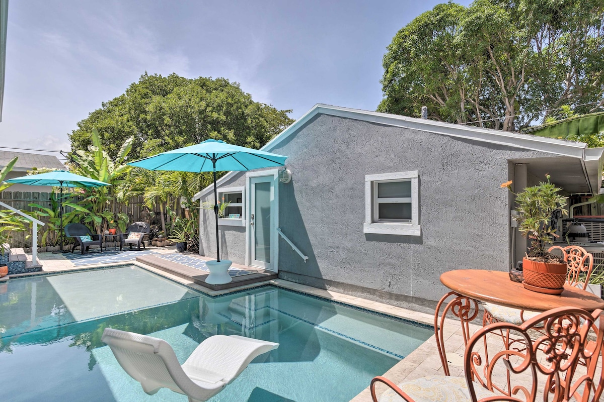 A landscaped outdoor area features a heated saltwater pool surrounded by lush tropical vegetation. Umbrellas provide shade over a dining table and a relaxing lounge chair is positioned at the water's edge, enhancing the serene ambiance of the space.
