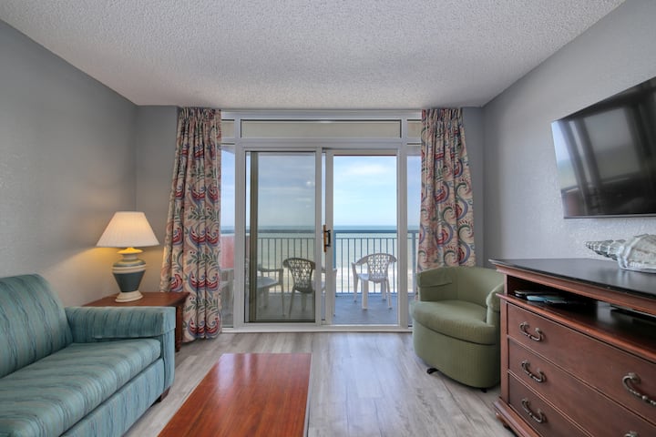 Dhomë ndenjjeje me divan gjumi, karrige ndenjjeje dhe televizor