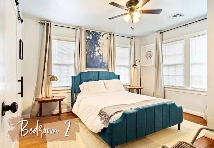 Une chambre confortable et sereine avec un lit queen size, deux tables de chevet et un tapis à motifs géométriques. Le lit est recouvert d'une couette blanche et d'oreillers, et il y a deux lampes sur les tables de nuit.