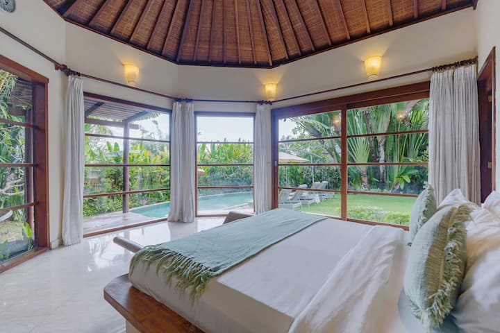 Panoramische hoek slaapkamer gevuld met natuurlijk licht en tropisch landschap.