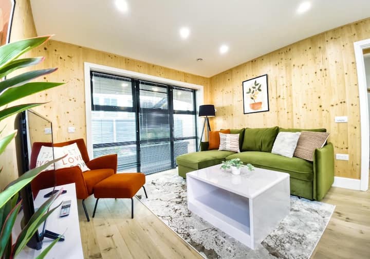 - Sala de estar luminosa y acogedora con un elegante sofá verde, paredes cálidas de madera y detalles vibrantes.
- Las ventanas del piso al techo invitan a la luz natural, mejorando el diseño ecológico.
- Perfecto para la relajación, con una decoración moderna y un ambiente relajante.