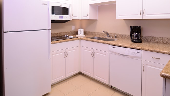 A kitchenette is equipped with white cabinetry and a granite countertop. Essential appliances include a refrigerator, microwave, and dishwasher. A coffee maker is positioned beside the sink, providing convenience for morning routines. Ample counter space allows for meal preparation.