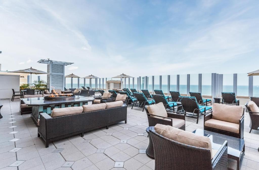 An outdoor deck area is observed, featuring multiple seating arrangements with soft cushions. Lounge chairs are positioned for relaxation, complemented by shaded umbrellas. The backdrop reveals panoramic ocean views under a clear blue sky, creating an inviting space for leisure and social gatherings.