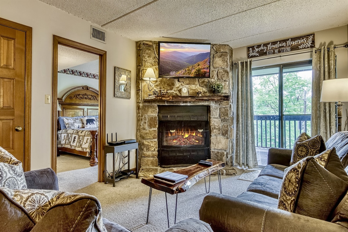 The family room features a stone fireplace with an electric insert, providing warmth and ambiance. A mounted television is positioned above the fireplace. Comfortable seating is arranged around, with a view through sliding glass doors leading to a patio, emphasizing the inviting atmosphere.
