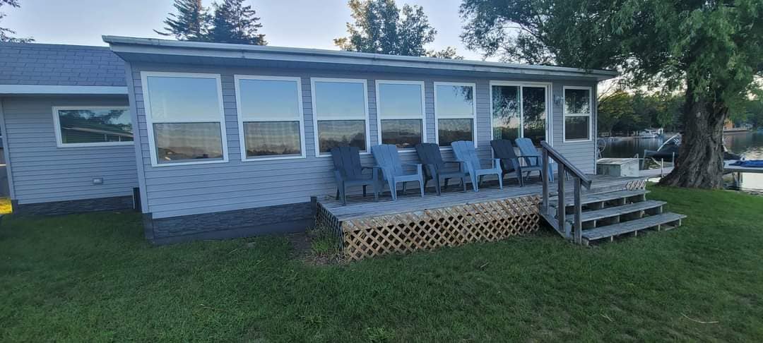 A sunporch is featured with multiple gray chairs arranged on a wooden deck, providing a comfortable space to enjoy views of Pratt Lake. Large windows allow natural light to flood the area, enhancing the connection to the outdoors.