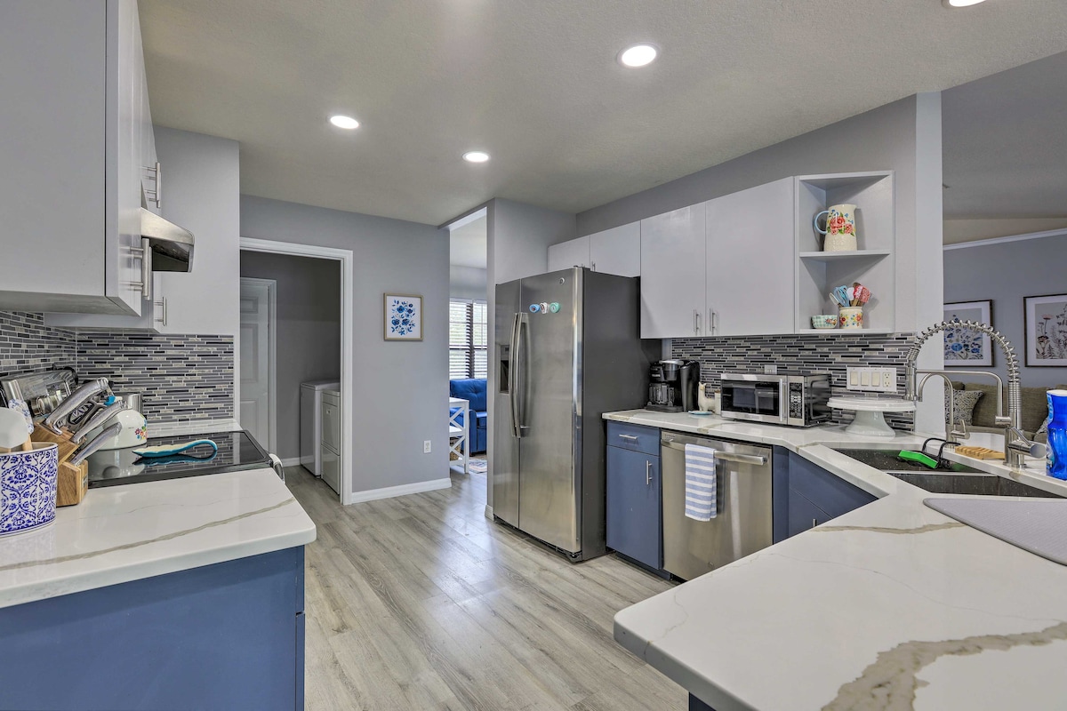 The kitchen features modern appliances including a stainless steel refrigerator, microwave, and oven. Gray cabinets and light countertops complement the mosaic tile backsplash. The layout includes a breakfast bar, ample counter space, and is well-lit with recessed ceiling lights.