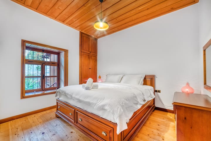 ห้องนอนสว่างและน่าอยู่พร้อมเตียงไม้เนื้อแข็ง ผ้าปูที่นอนนุ่ม และการตกแต่งด้วยวัสดุธรรมชาติที่ให้ความรู้สึกอบอุ่น หน้าต่างบานใหญ่ช่วยให้แสงสว่างอ่อนๆ ส่องเข้ามาและมองเห็นวิวสวน ทำให้ที่พักเงียบสงบและผ่อนคลายหลังจากออกไปข้างนอกมาทั้งวัน