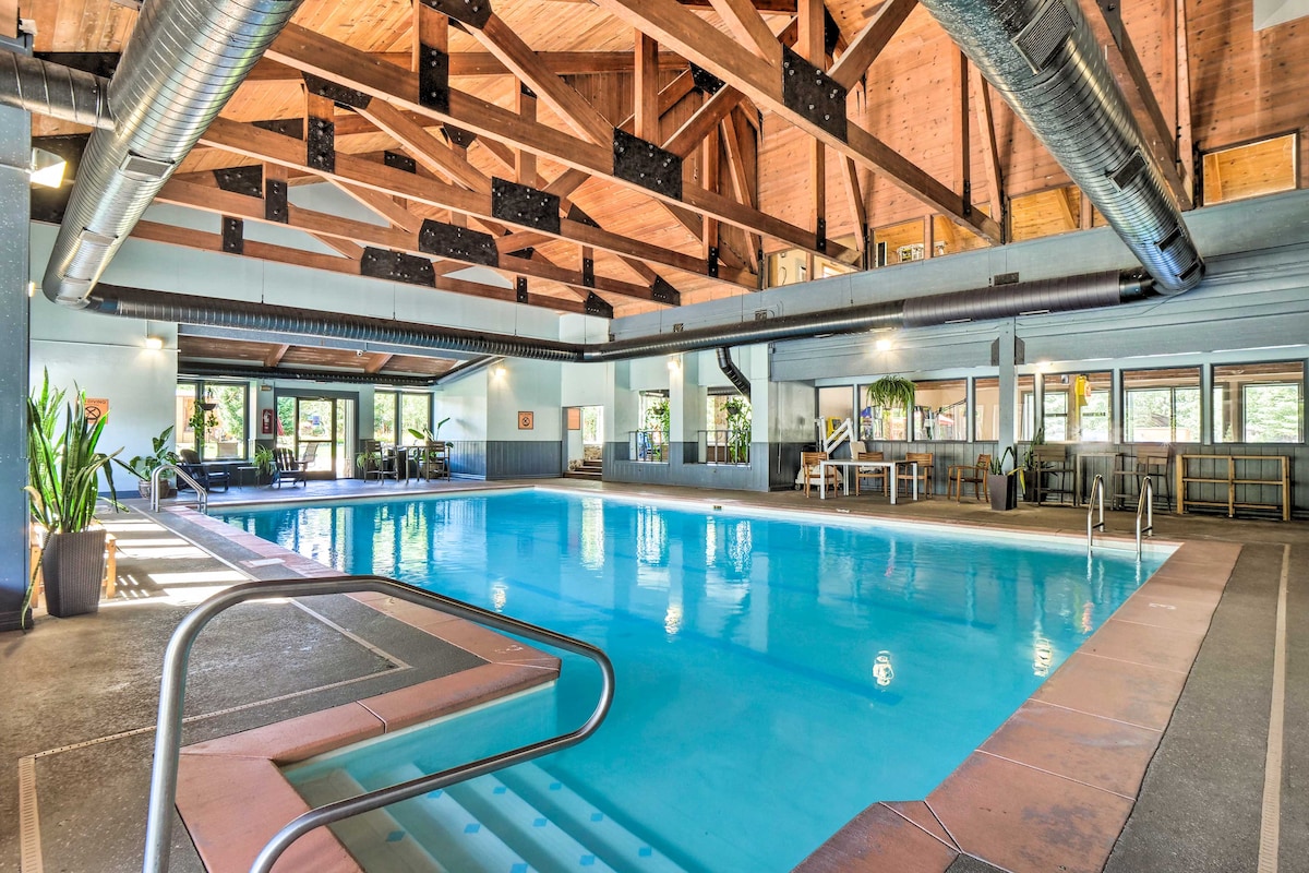 An indoor heated pool area is highlighted by vaulted wooden ceilings and large windows, allowing natural light to fill the space. Relaxing seating is available nearby, and potted plants add a touch of greenery to the inviting atmosphere.