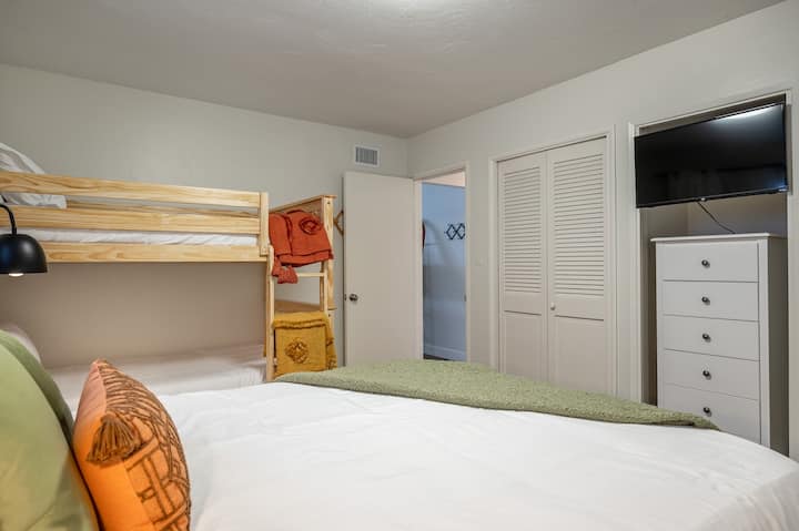 Habitación con litera para huéspedes con literas individuales y cama tamaño queen independiente, TV y vestidor.