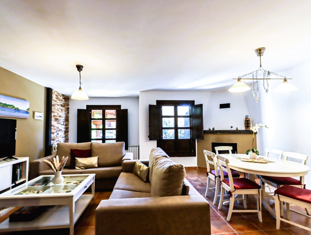 A spacious living area is highlighted by a comfortable sofa and elegant coffee table. Windows with wooden shutters allow natural light to fill the room. A dining table with chairs is positioned nearby, creating a welcoming space for dining and relaxation.