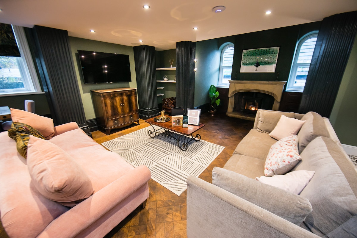 The living area features a blend of modern and classic design elements. A comfortable pink sofa and a neutral grey sofa are arranged around a central coffee table. A TV is mounted on the wall, and a fireplace adds warmth to the space. Soft lighting enhances the serene atmosphere.