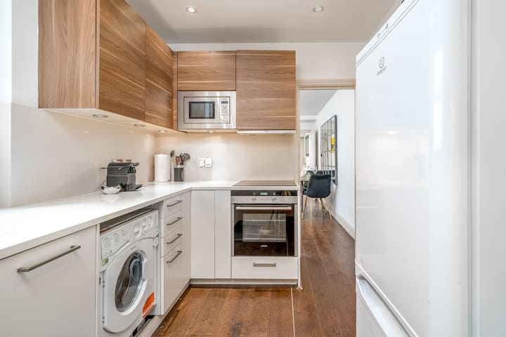 Die Küche verfügt über elegante weiße Arbeitsplatten und Ahorn-Overhead-Schränke, die eine saubere und moderne Ästhetik bieten. Der Induktionsherd bietet ein präzises und effizientes Kochen, mit dem du deine Lieblingsgerichte mit Leichtigkeit zubereiten kannst. 