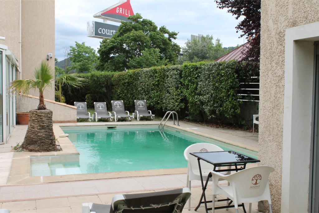 An outdoor swimming pool is surrounded by a tiled patio, featuring lounge chairs for relaxation. Lush greenery is visible along the perimeter, providing a sense of privacy. The pool area is well-lit, inviting guests to enjoy the space.