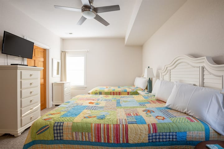 Dormitorio con cama tamaño queen y dos camas individuales con baño comunicado, TV, ventilador de techo y tocador