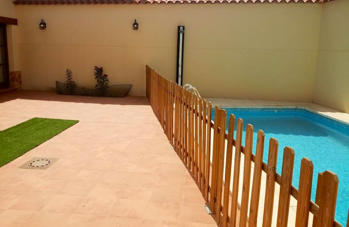 A private pool is visible within a fenced area, accompanied by a well-maintained patio surface. A small strip of grass is located beside the pool area. Soft lighting fixtures can be seen mounted on the wall, providing ambient illumination for evening relaxation.