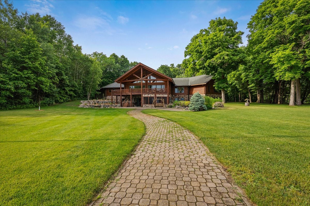 A spacious lodge is shown surrounded by lush greenery, with a well-maintained stone pathway leading up to the entrance. Large windows create a welcoming ambiance, and the expansive lawn provides ample space for outdoor activities.