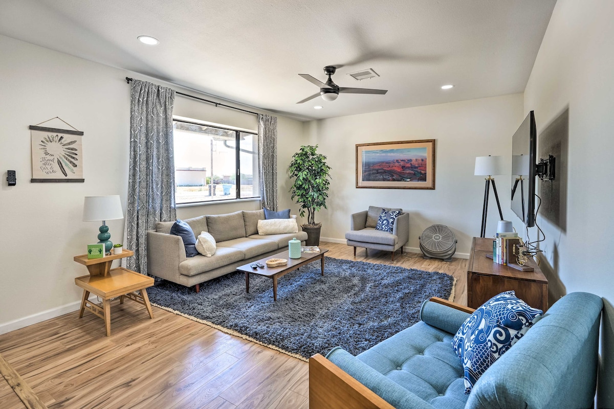 A spacious living area is highlighted by natural light from a large window. Comfortable seating options include a grey sofa, a blue armchair, and a wooden coffee table. Decorative elements include a potted plant, wall art, and a cozy area rug enhancing the inviting atmosphere.