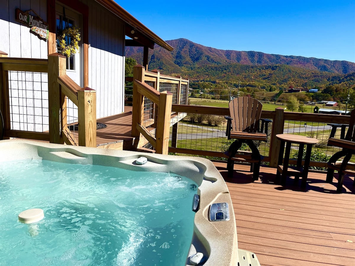 A hot tub is positioned on a spacious deck, surrounded by wooden railings. Comfortable Adirondack chairs face a panoramic view of the rolling hills and vibrant autumn foliage stretching across the landscape.