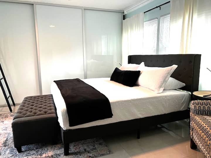 พักผ่อนอย่างสบายใจในห้องนอนหลักที่มีเตียงคิงไซส์และทางเดินตรงไปยังระเบียงกลางแจ้ง พร้อมด้วยโต๊ะทำงานอัจฉริยะ โซฟาเก้าอี้ พัดลมติดเพดาน และตู้เสื้อผ้า