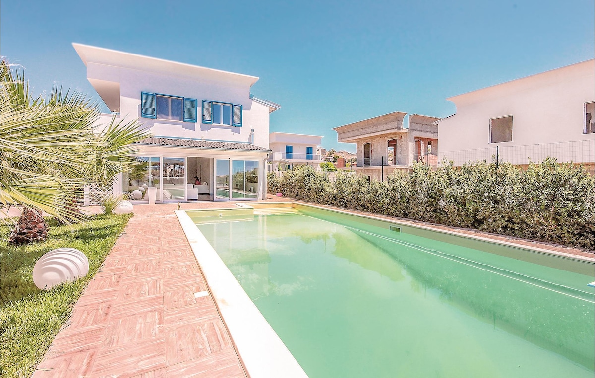 A modern villa is depicted, featuring a spacious private pool surrounded by a lush lawn. Light-colored tiles lead toward the pool, and large glass doors provide views into the interior. The surrounding greenery and bright blue sky create a serene outdoor environment.
