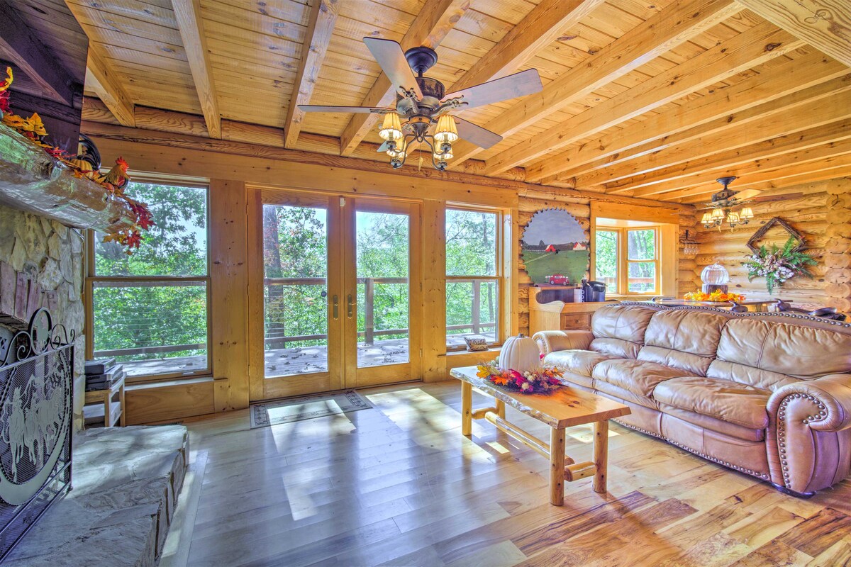 A spacious living area features warm wood ceilings and walls. A large leather sofa is arranged around a wooden coffee table. Glass doors open to outdoor views, while a decorative fireplace adds a cozy touch. Natural light enhances the room's inviting atmosphere.
