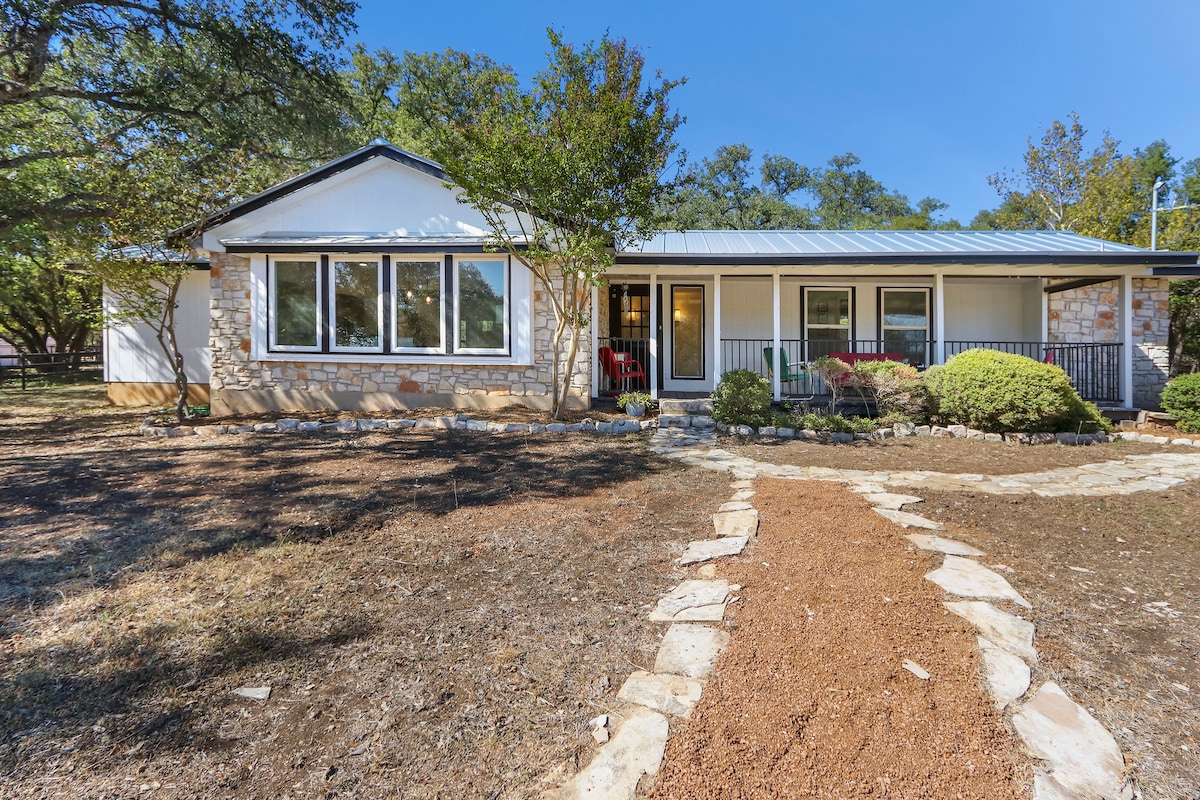The exterior of the cottage features a welcoming front porch, framed by native landscaping and mature oak trees. A stone pathway leads to the entrance, inviting guests to enjoy the views of the surrounding hill country. Large windows allow natural light to fill the front of the home.