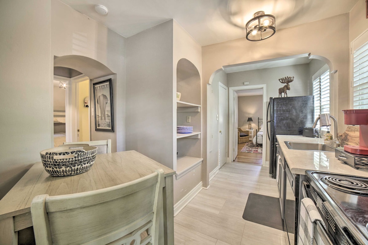 The kitchen showcases a welcoming space with light-colored cabinetry and a dining table. Modern appliances are present, including a refrigerator and stove. Shelves hold neatly arranged items, while windows allow natural light to illuminate the area. The adjacent archway leads to other parts of the home.