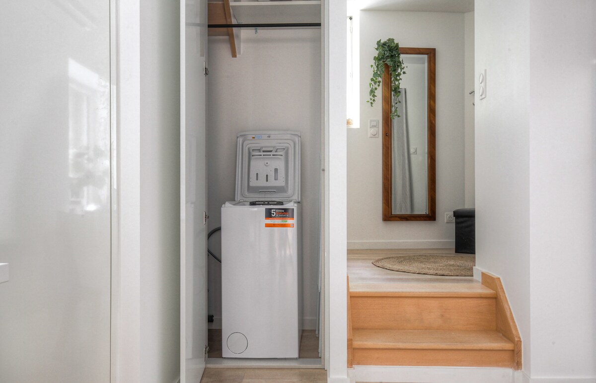 A laundry area is presented, featuring a stacked washing machine and dryer unit. A stylish full-length mirror is mounted on the wall beside the unit, while steps lead up to another level. A small area rug is placed on the floor, adding a touch of warmth.