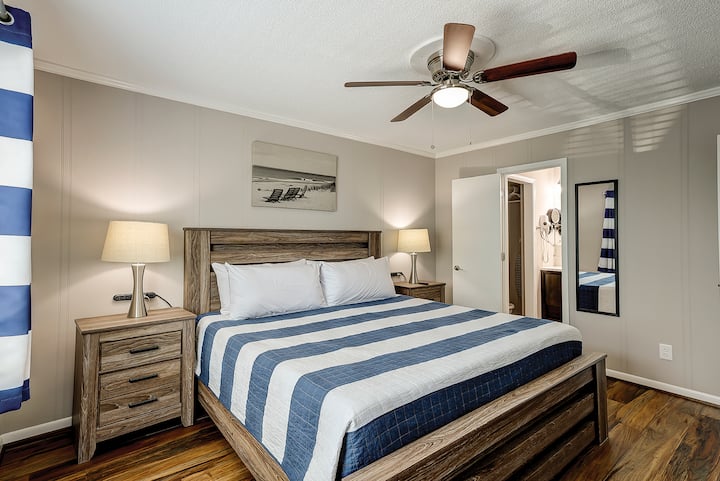 Chambre principale avec lit King Size et salle de bain privée complète. Dispose de 2 tables de nuit avec lampes et multiprises, d'une commode de grande taille, d'une télévision Roku, d'un réveil, d'un ventilateur de plafond et d'une porte d'accès au balcon.