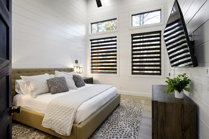 Dormitorio privado tamaño king con vistas a los árboles y ropa de cama de apoyo pero acogedora