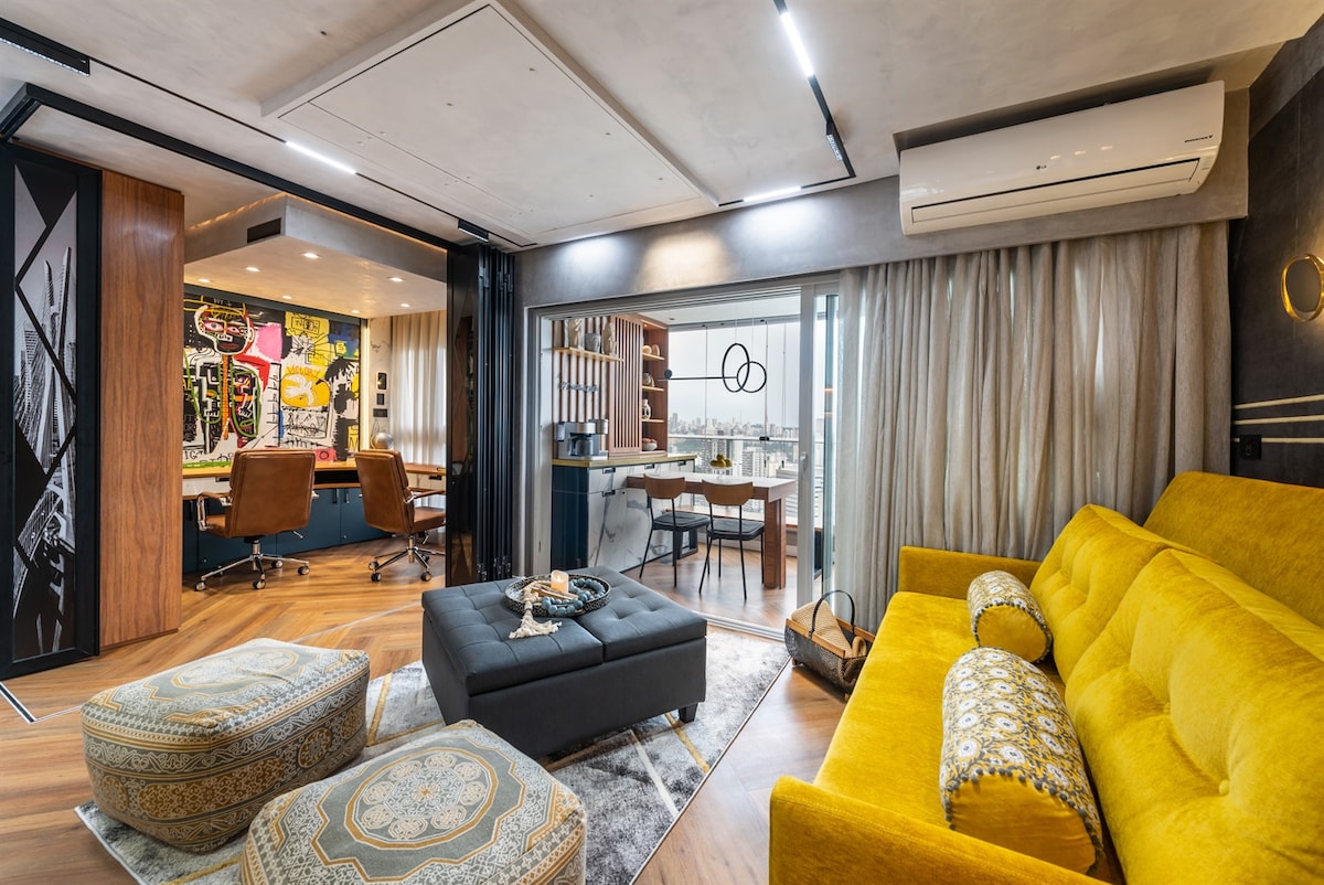 Chumba cha kisasa, rangi za hali ya juu na mahiri zilizo na sofa na puff za ziada, na ofisi ya nyumbani iliyo na kaunta na kiti cha ngozi kwa watu wawili.